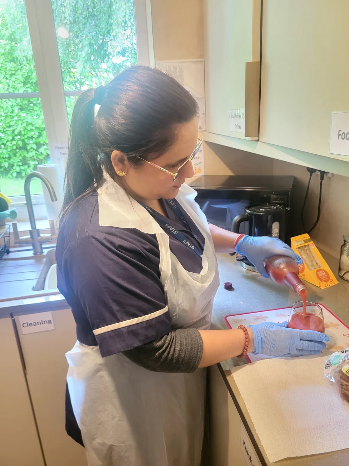 Care4Us carer in apron and gloves preparing a drink in a client's kitchen during a home care visit